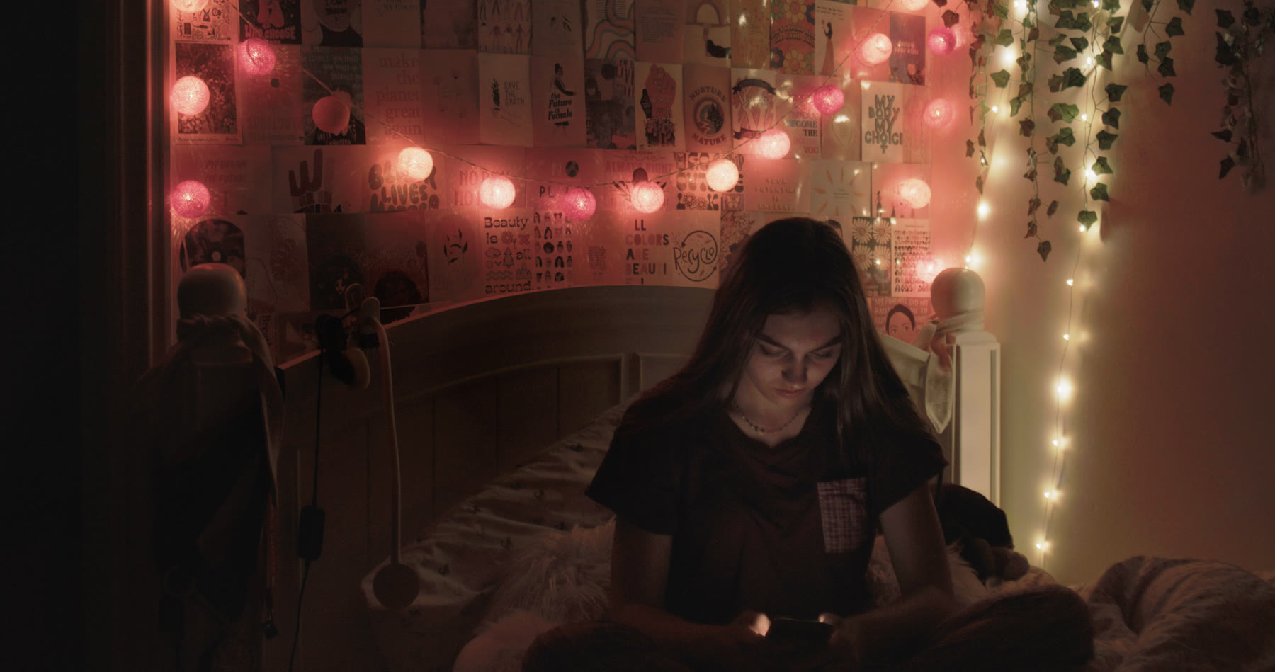 A young woman sits on her bed at night, lit by her phone